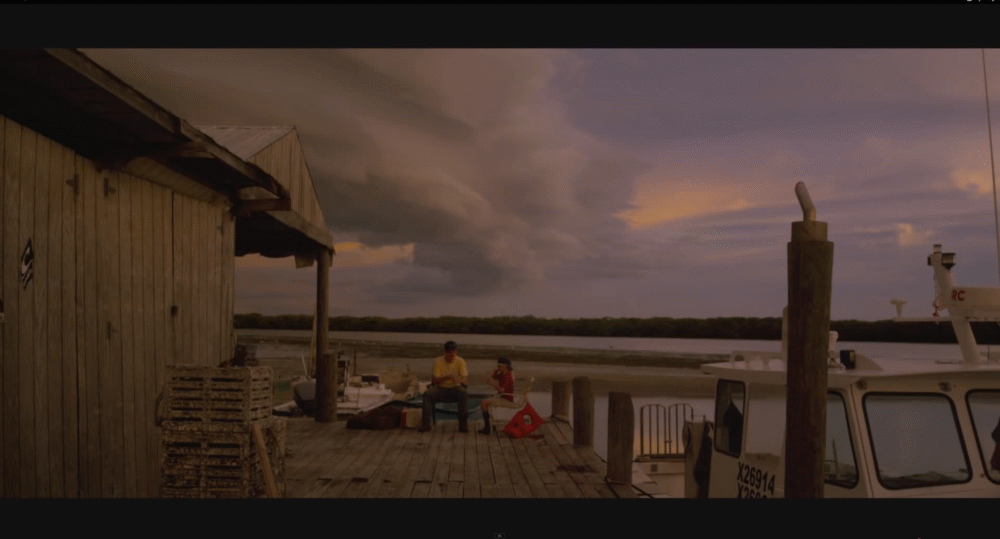 People on a dock in Paradise, FL, with boats and a dramatic sky at sunset.