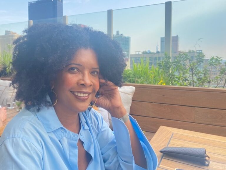 Paula Puryear smiling outdoors with city buildings in the background.