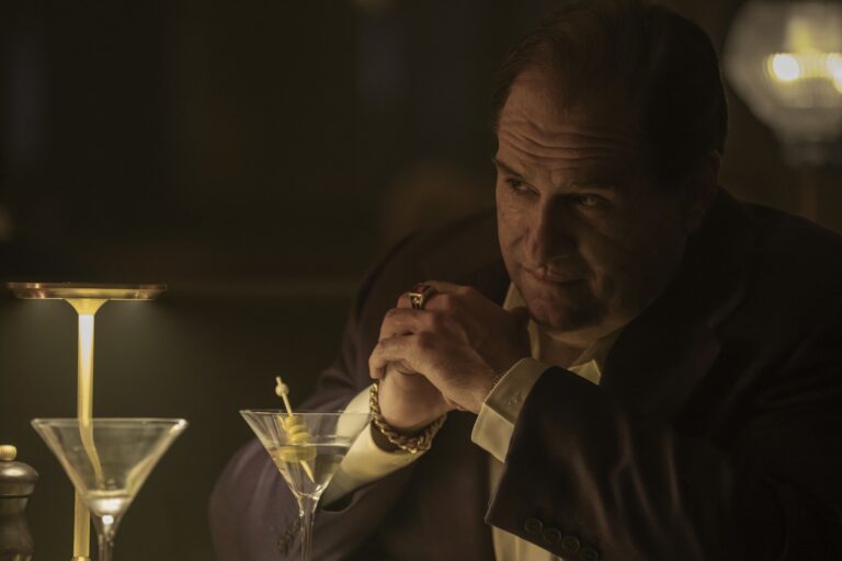 Colin Farrell as The Penguin, sitting at a table with a martini.
