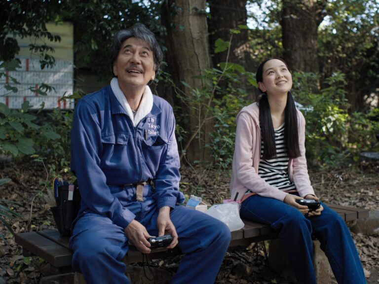 Perfect Days film still: Man and young woman on a park bench, looking up.