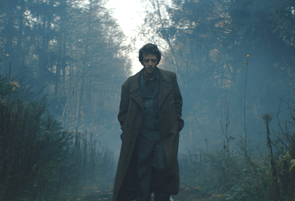 Man in coat walks through misty forest.