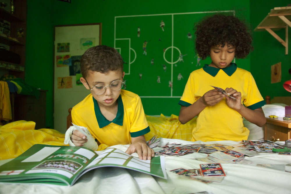 Two boys in yellow soccer jerseys sorting Maradona cards. Soccer field drawn on the green wall.
