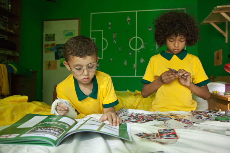 Two boys in yellow soccer jerseys sorting Maradona cards. Soccer field drawn on the green wall.