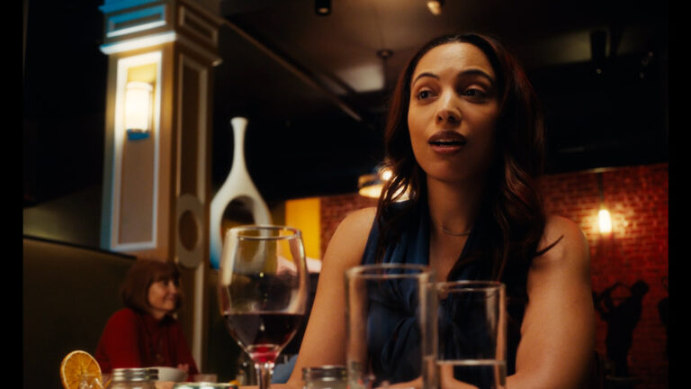 Woman at restaurant table with wine glasses, possibly discussing "At Capacity.