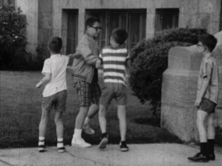 Boys in shorts and socks play near a building, possibly related to "When We Were Bullies.