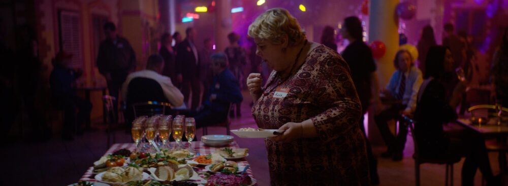 Woman at buffet with "Anna" name tag in a crowded party.