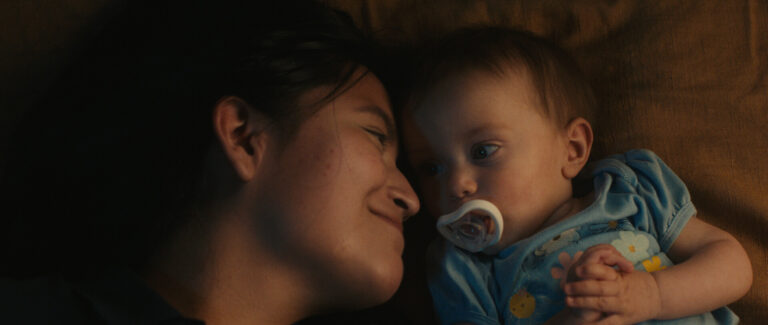 Mother lovingly gazes at her baby with a pacifier. Intimate, tender moment.