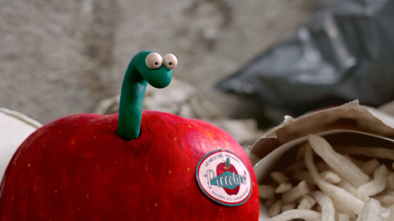 Claymation of Piccolino apple with a green worm emerging, sticker reads "Piccolino