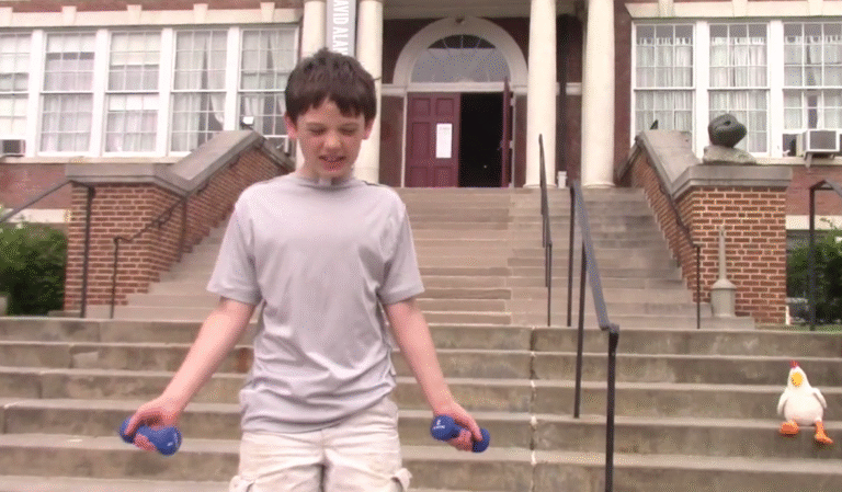 Boy exercising with dumbbells outside McGuffey Art Center, with a chicken plush toy sitting on the stairs nearby.