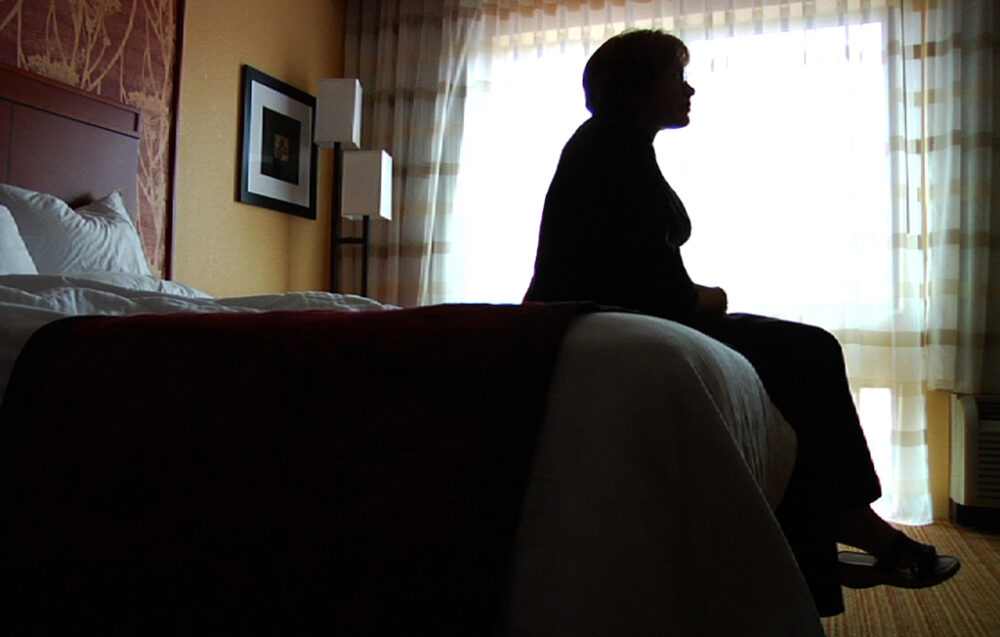 Silhouette of a woman sitting on a hotel bed, looking out the window.