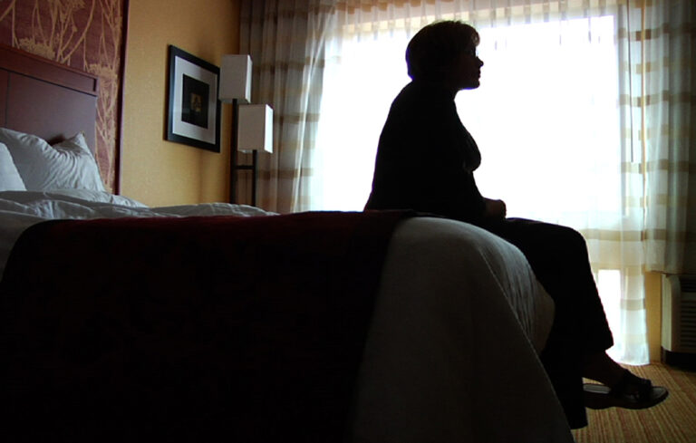 Silhouette of a woman sitting on a hotel bed, looking out the window.