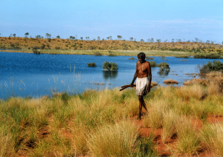 Aboriginal man walking by a lake in the Australian outback, reflecting the themes of "Putuparri and the Rainmakers"