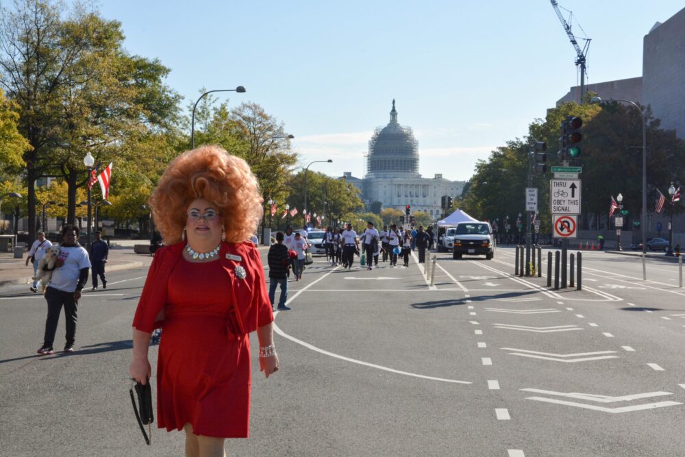 Drag queen in a red dress walks toward the US Capitol Building, part of the "Queen of the Capital" event.