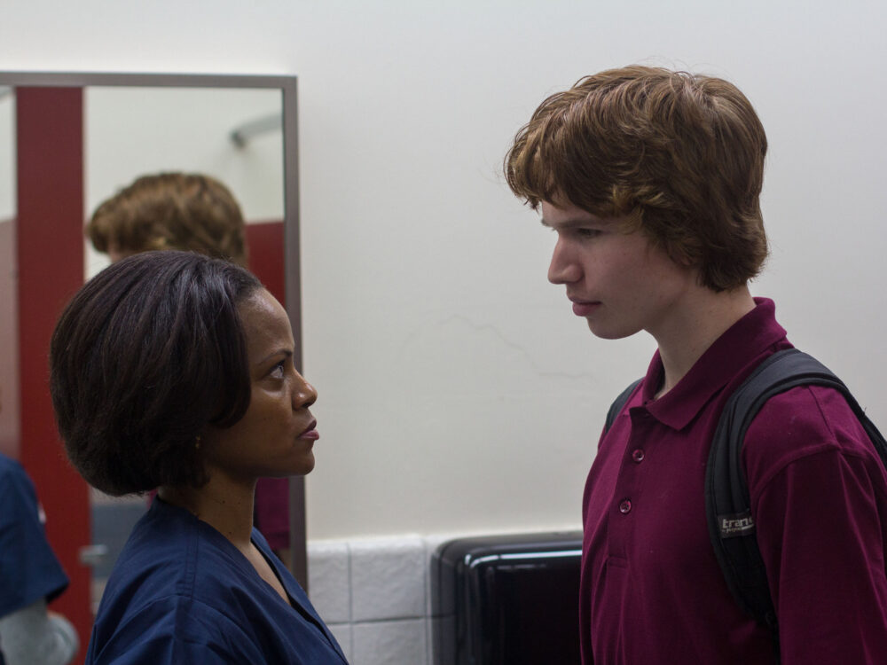 Young man in maroon polo confronting a nurse.