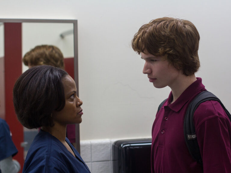 Young man in maroon polo confronting a nurse.