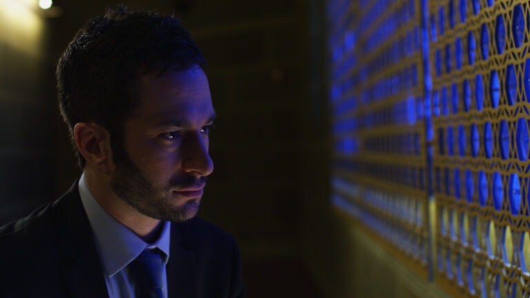 Man in suit looks thoughtfully at illuminated wall.