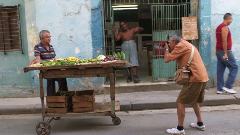 Cuban street scene: Man photographs fruit vendor near a shop, evoking Walker Evans' style in "Return to Cuba"
