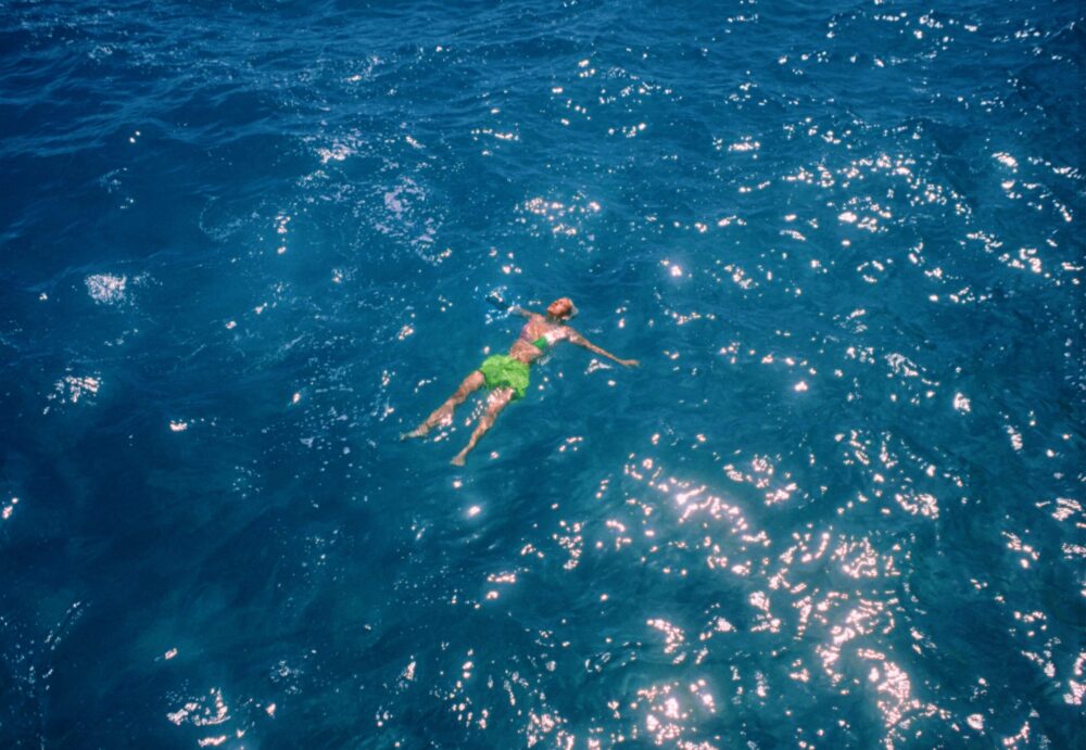 Person floating in deep blue ocean water, sun reflecting on the surface.