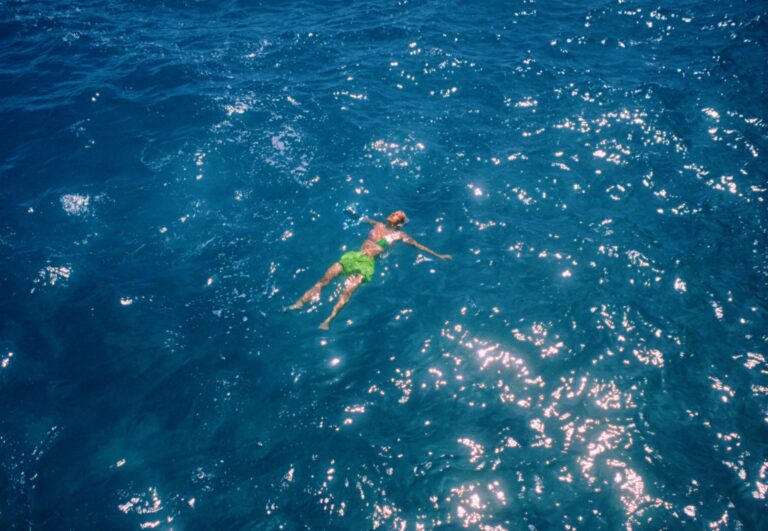 Person floating in deep blue ocean water, sun reflecting on the surface.