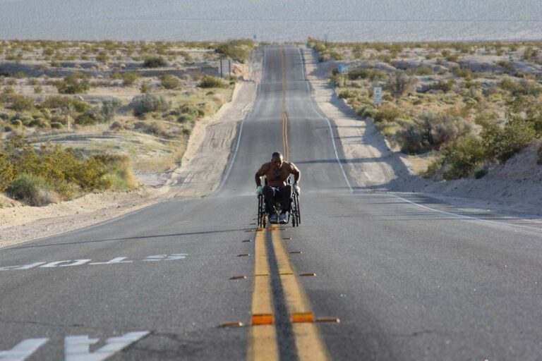 Man in wheelchair races on a long desert road.