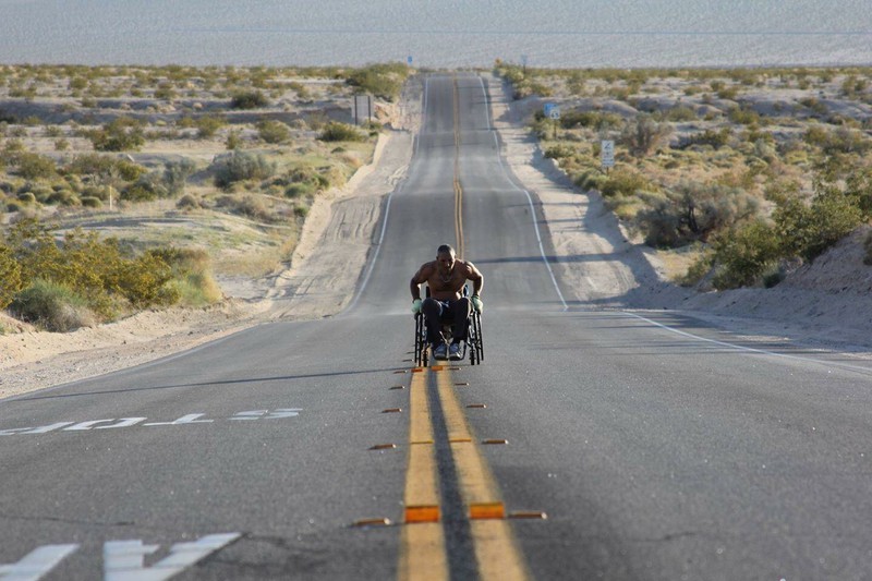 Man in wheelchair races on a long desert road.