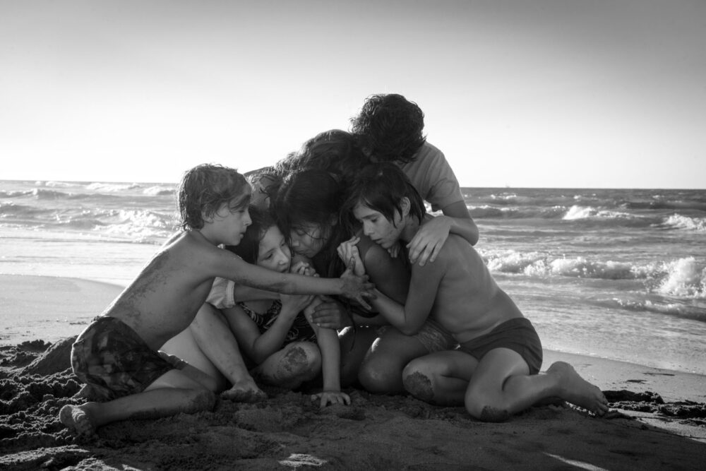 Children huddled together on a beach near the ocean. Scene from the film Roma.