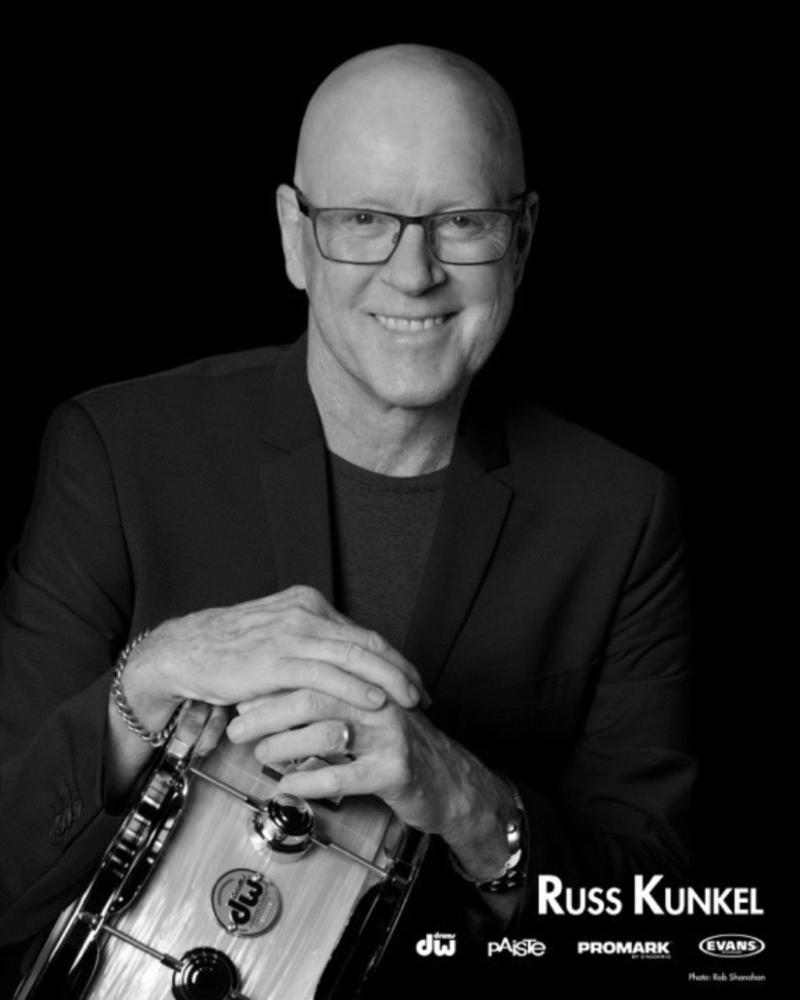 Russ Kunkel, drummer, smiling with drum and logos for DW, Paiste, Promark, and Evans.