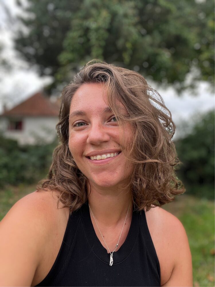 Ruthie Petitto smiling outdoors with a house and trees in the background.