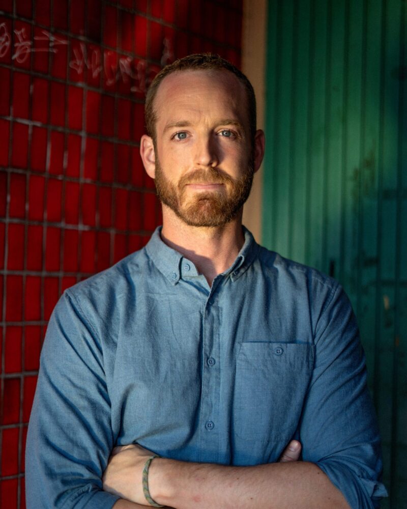 Portrait of Scott Faris with arms crossed, standing in front of a red and green wall.