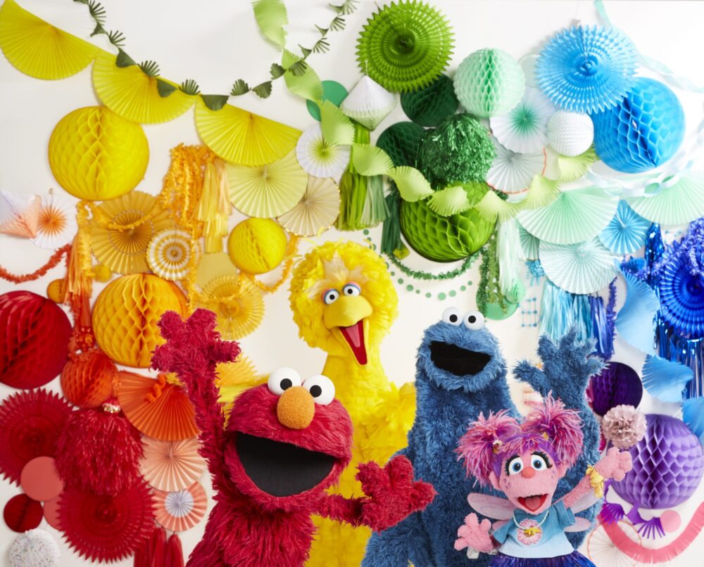Sesame Street characters Elmo, Big Bird, Cookie Monster, and Abby Cadabby with colorful decorations.