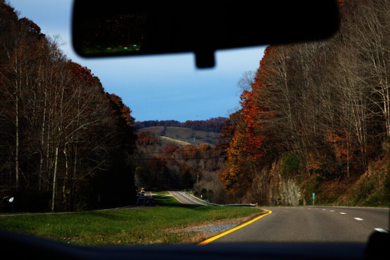 Autumn road trip view through a car windshield, showcasing fall foliage and winding highway.