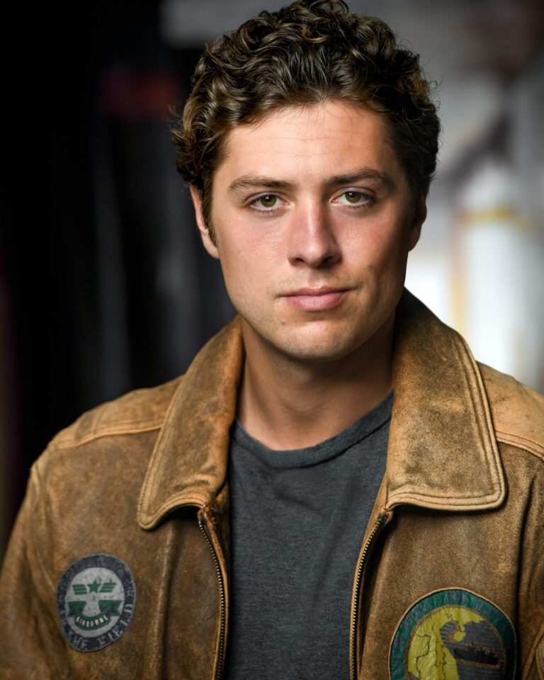 Sam Brooks headshot, wearing a leather jacket with patches. Actor portrait.
