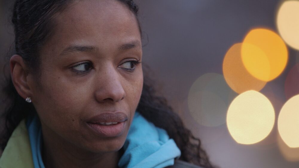 Pensive Black woman with city lights bokeh in background.