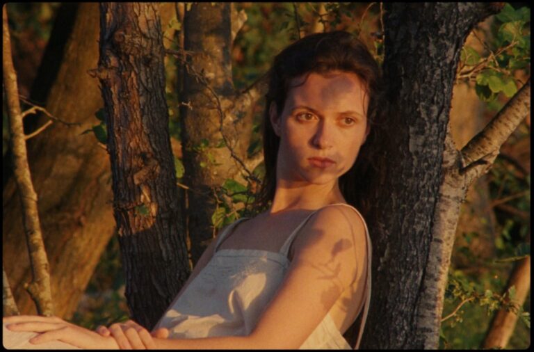 Woman in white dress amongst trees, bathed in golden light.