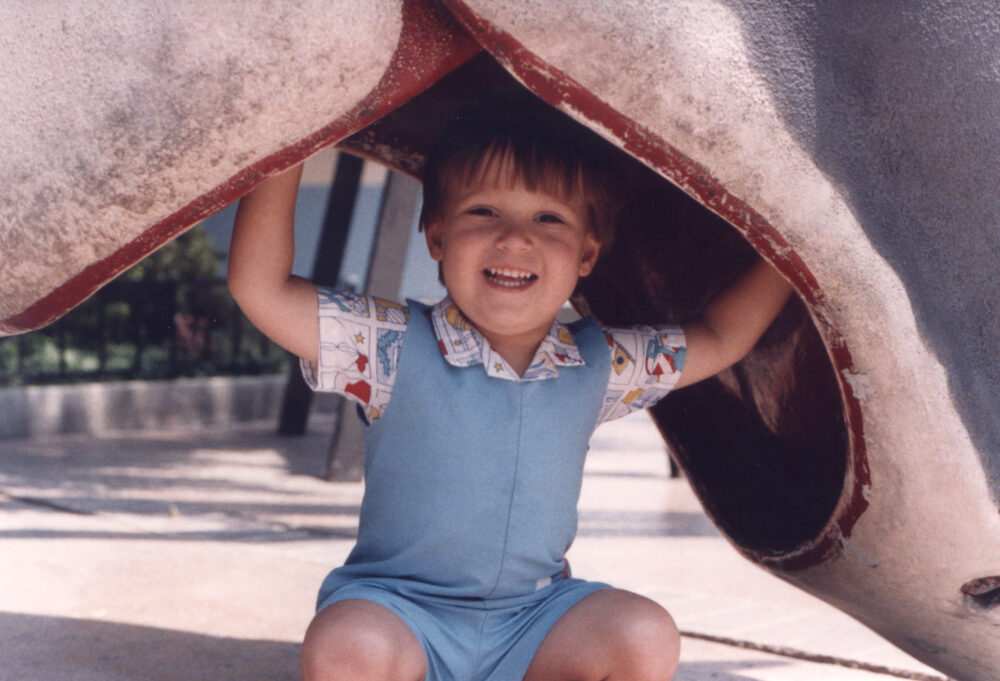 Smiling child plays under an elephant statue, enjoying scenes with Ivan.