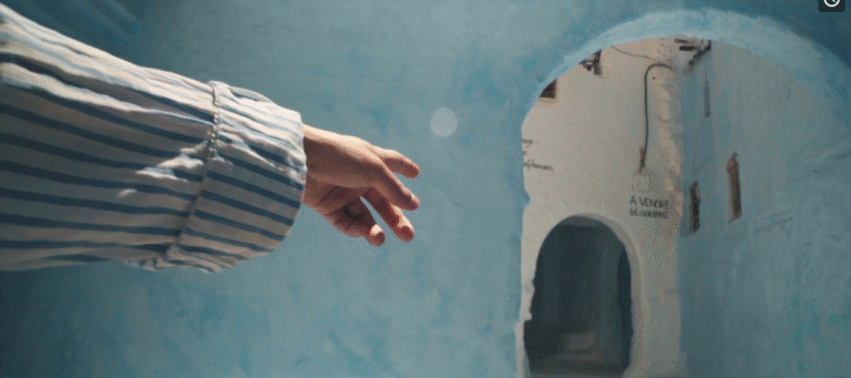 Hand reaching towards a blue alleyway with "A Vendre" (For Sale) sign in a Moroccan town.