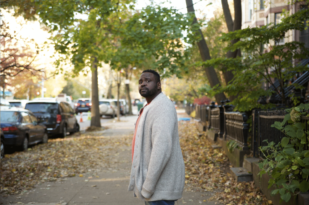 Man in cardigan on sidewalk covered in leaves, looking back.