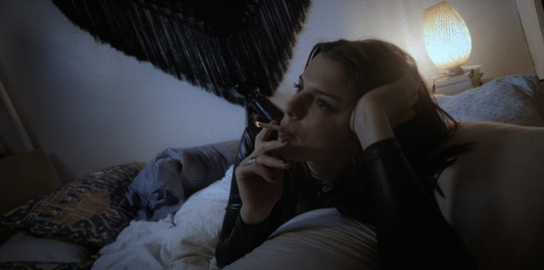 Woman smoking on bed in a dimly lit room.