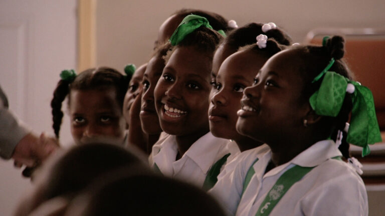 Smiling Haitian schoolgirls in uniforms with green ribbons.