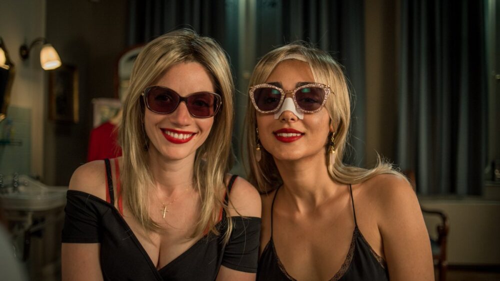 Two women wearing sunglasses and bandages after plastic surgery.