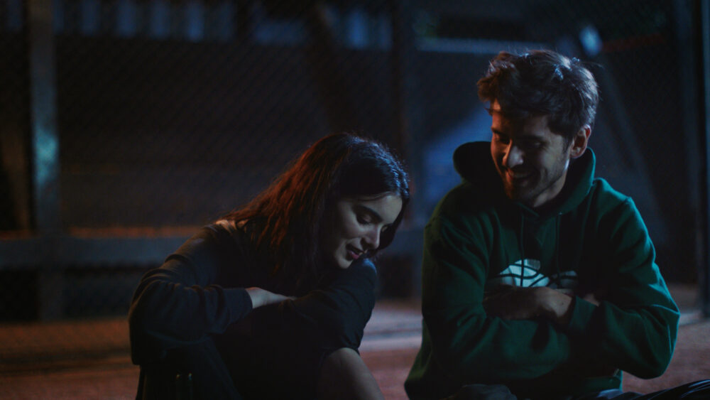 Two young people, possibly from the movie Shithouse, sitting and talking outdoors at night.