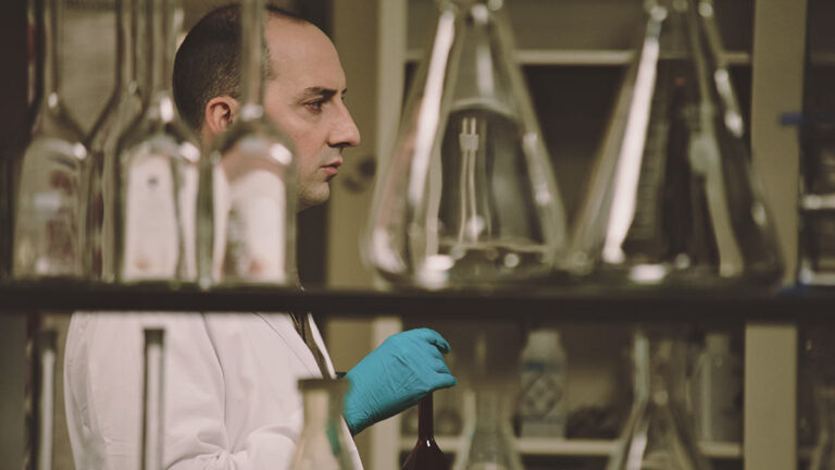 Scientist in lab coat holding beaker, surrounded by lab equipment.