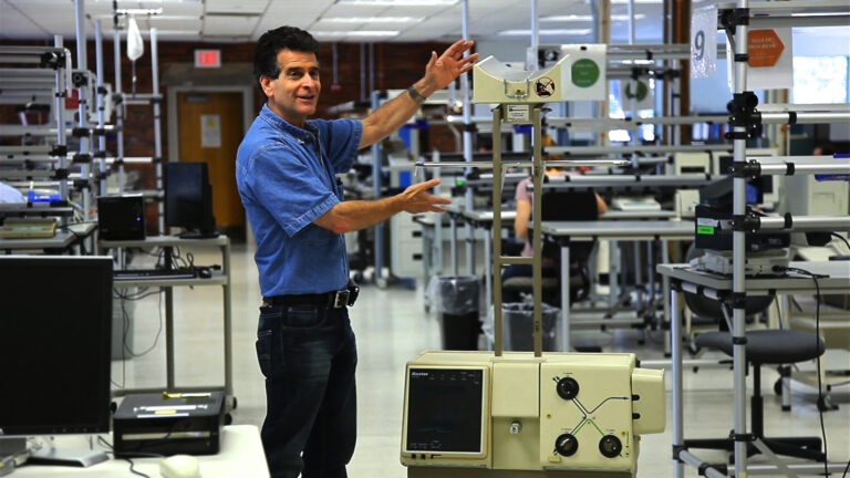 Man explaining a Baxter slingshot testing machine in a lab environment.