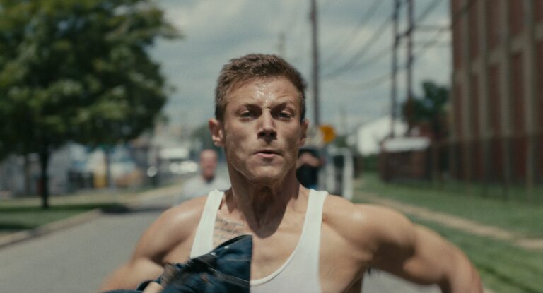 Man running in Sollers Point, wearing a tank top and holding jeans.