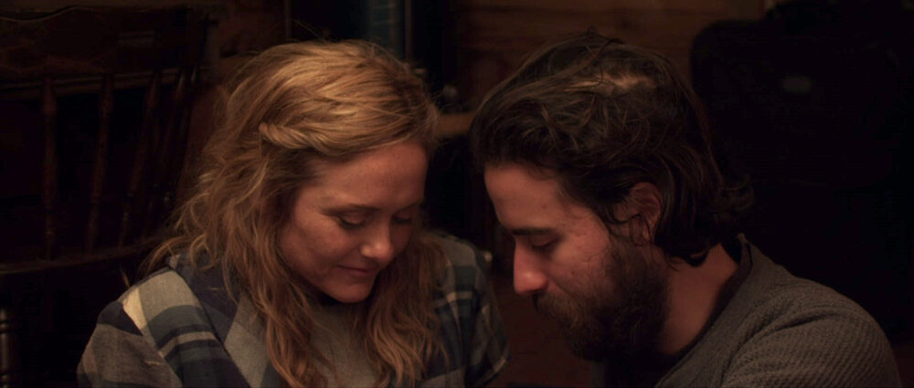 Couple in "Some Beasts" movie, looking down. Woman with blonde hair, man with beard.