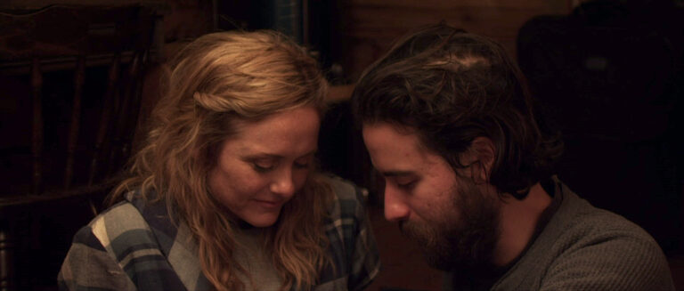 Couple in "Some Beasts" movie, looking down. Woman with blonde hair, man with beard.