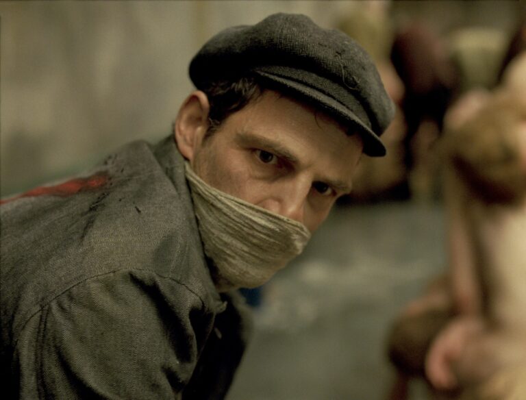 Son of Saul: A man with a cap and face covering looks intensely at the camera.