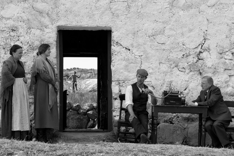Scene from "Song of Granite" film: People outside old stone house, man on phone.