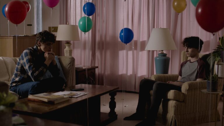 Two young men sit in a room decorated with balloons in "Stay Awake".