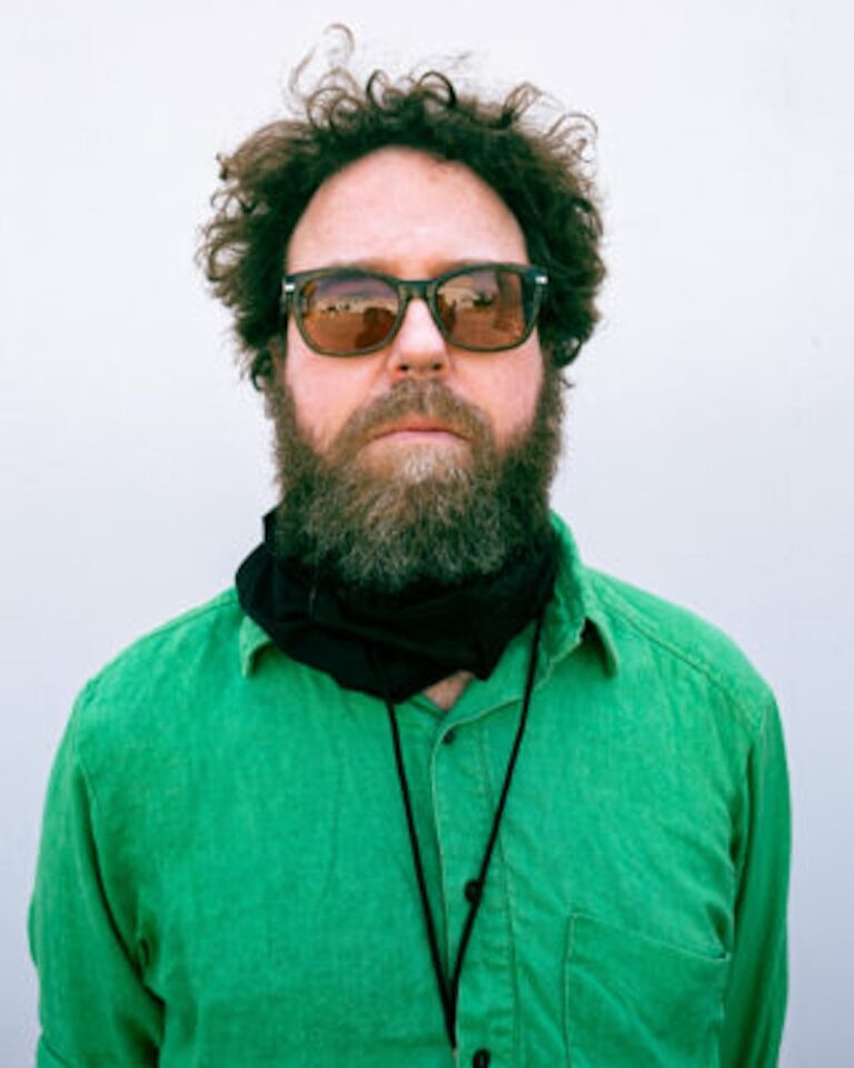 Steve West, musician with curly hair, beard, green shirt, and sunglasses.